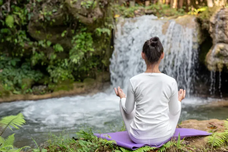 Woman sitting peacefully beside a waterfall in a calming natural setting