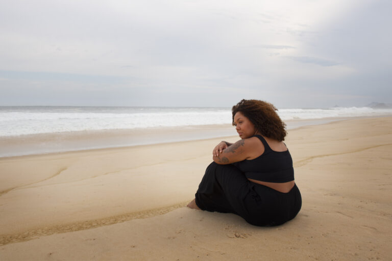 Woman sitting alone on a quiet beach, hugging her knees and looking overwhelmed – representing emotional overload and ADHD burnout.