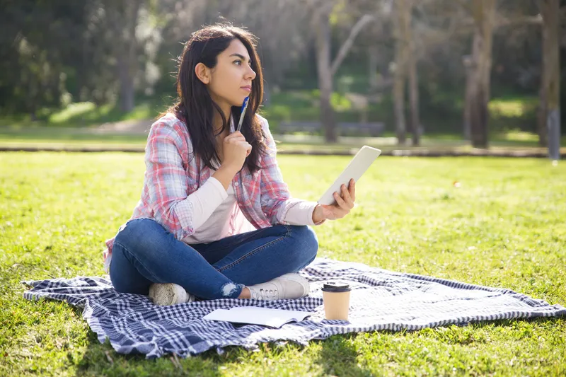 Woman sitting outdoors using a tablet in a calm park setting