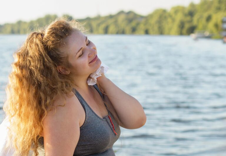 Woman with ADHD outdoors by the water, resting after exercise with a towel on her shoulder – reflecting hormone-related energy shifts and self-care.