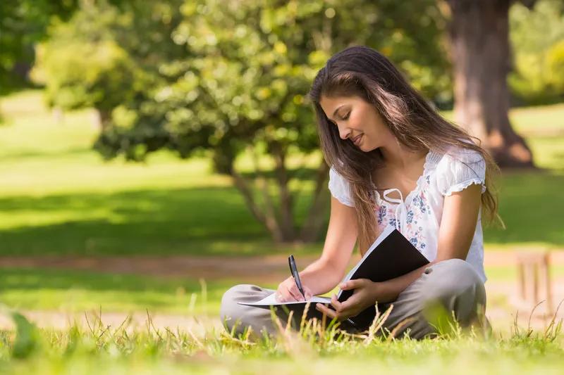 Woman sitting outdoors writing in a notebook, representing self-reflection, self-praise, confidence building, and positive self-worth with ADHD.