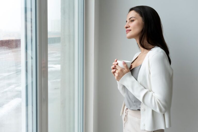 Woman standing at window, gently reflecting – symbolising calm and clarity in ADHD coaching for women