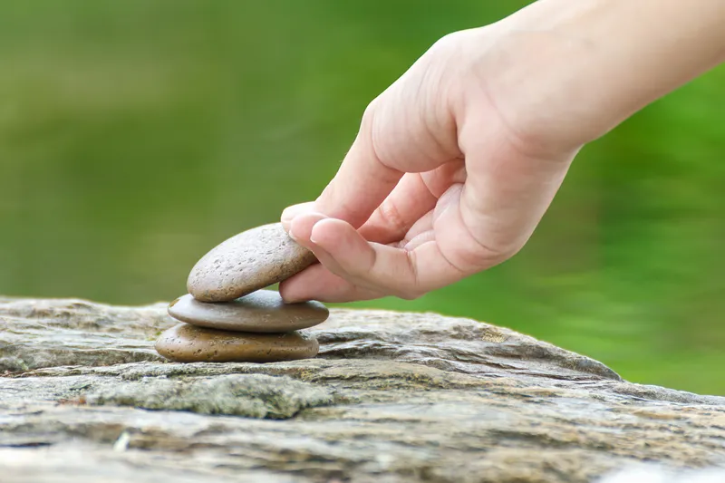 A close-up of a hand carefully balancing stones, representing the gradual process of rebuilding self-trust and confidence with ADHD.