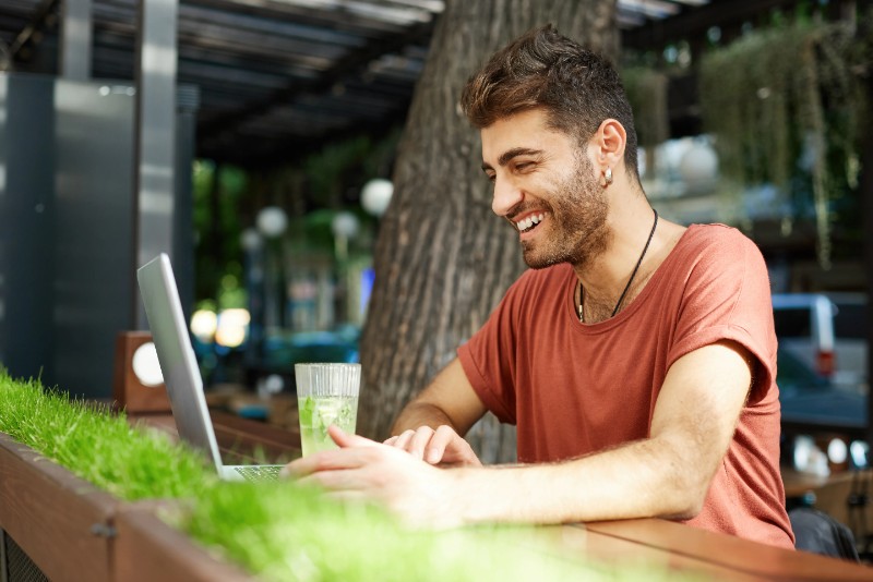 Smiling student using a laptop outdoors in a relaxed setting