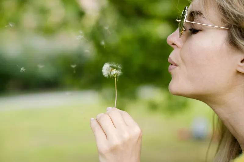 A close-up of someone blowing a dandelion, representing the small shifts in awareness and self-acceptance that can make life easier with ADHD.