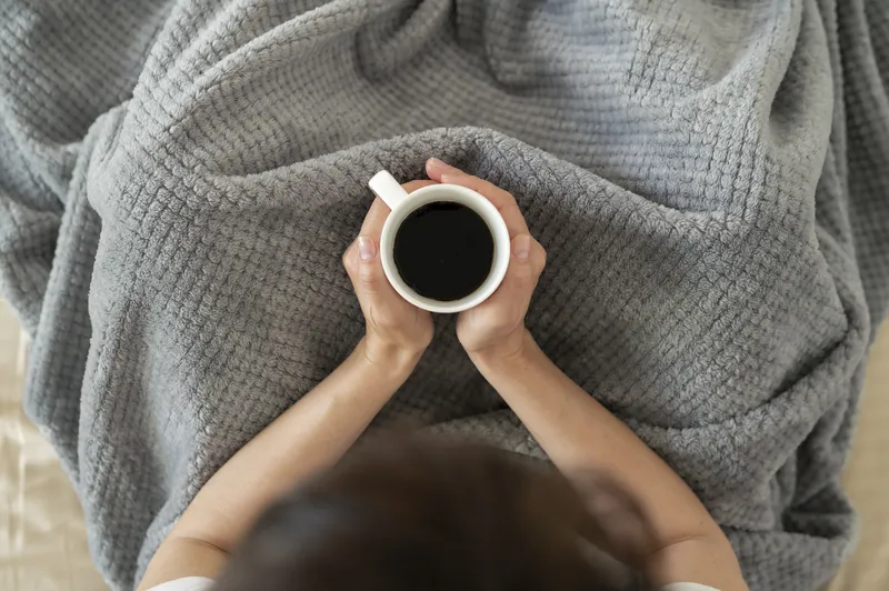 A close-up of someone sitting with a warm drink, representing the feeling of being mentally stuck and unable to get started with ADHD task paralysis.