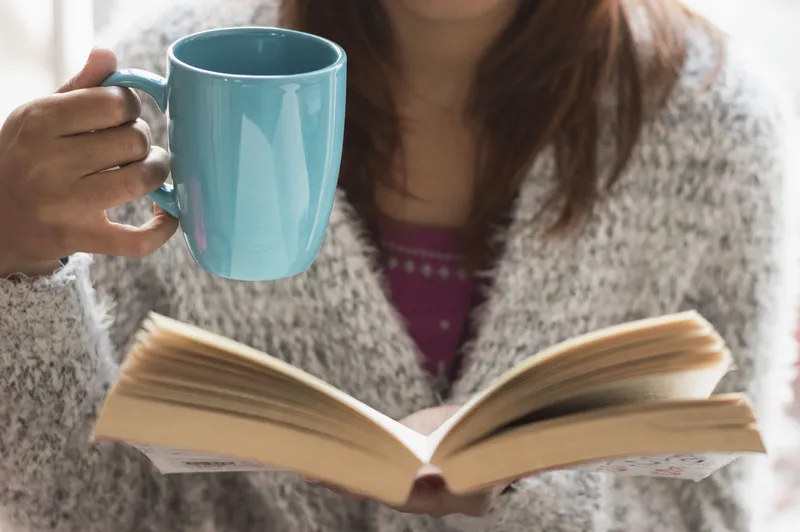 A close-up of someone holding a warm drink while reading, representing the experience of trying to relax when an ADHD brain feels wide awake despite exhaustion.