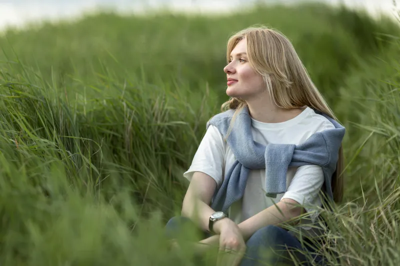 Woman relaxing in long grass outdoors reflecting calmly during ADHD coaching support journey