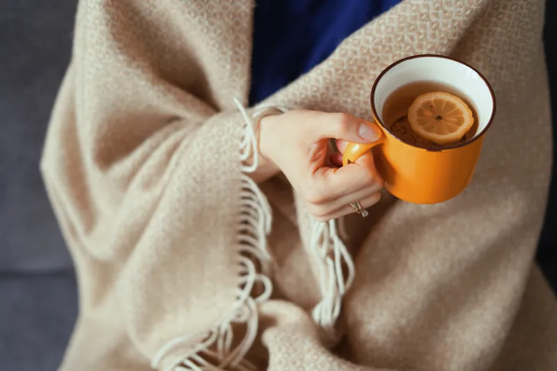 A close-up of someone wrapped in a blanket holding a warm drink, representing the emotional and physical impact of ADHD and hormones.