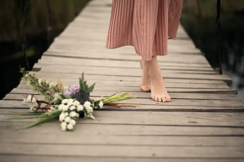 Woman walking barefoot holding flowers, reflecting on ADHD and self-compassion.