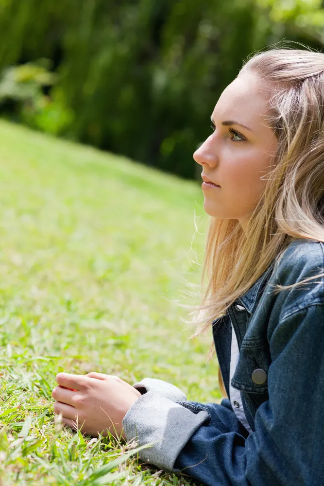A young woman lying on grass looking thoughtfully ahead, representing a calm and reflective space